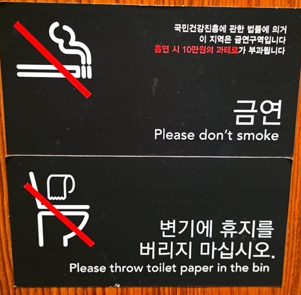 Sign prohibiting smoking and instructing to throw toilet paper in the bin, featuring graphics and bilingual text.