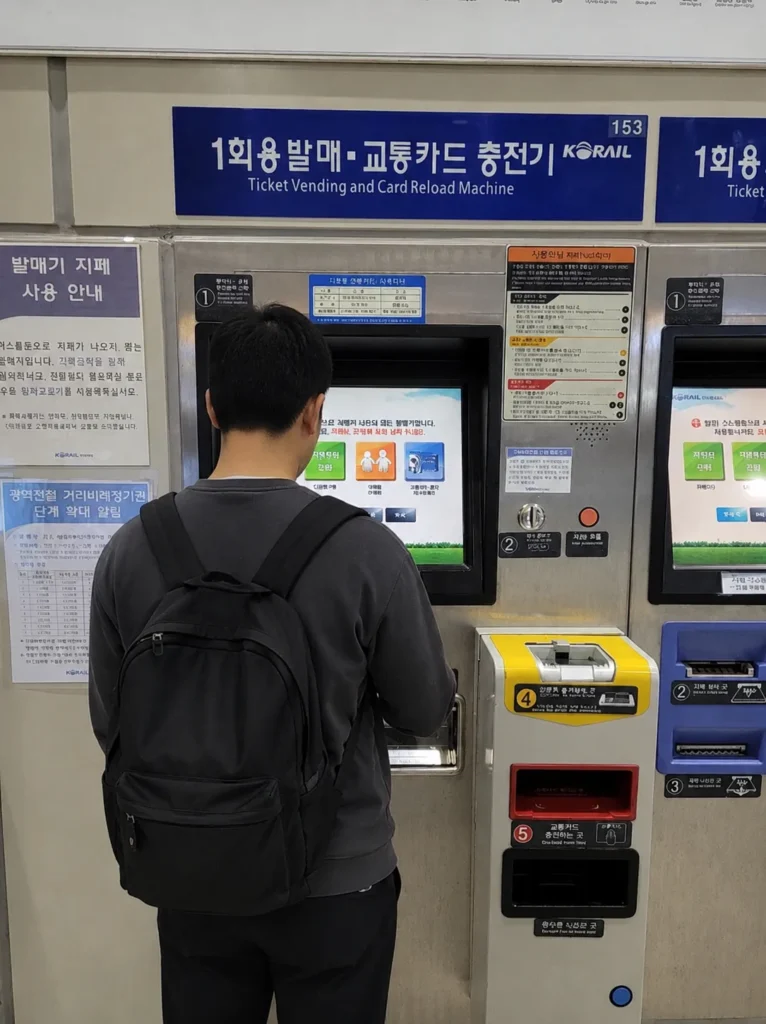 An adult stands at a Korail ticket vending and transit card reload machine.